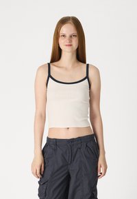 Bežs ribots īsās piedurknes tops ar tumši zila plecu siksnām, ar apaļu kakla izgriezumu. Apvienots ar tumšiem cargo biksēm ar sānu kabatām un pogu aizdari.