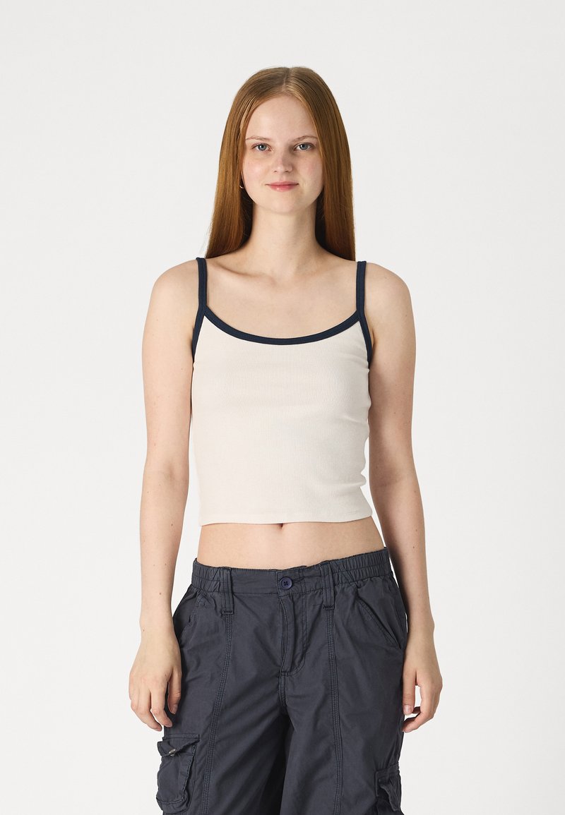 Bežs ribots īsās piedurknes tops ar tumši zila plecu siksnām, ar apaļu kakla izgriezumu. Apvienots ar tumšiem cargo biksēm ar sānu kabatām un pogu aizdari.