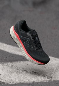 Schwarzer Sportschuh mit strukturiertem Obermaterial, pink-weiße Sohle, mit einem auffälligen Logo und Schnürdesign.