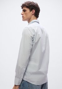 Vaaleanharmaa pitkähiha paita, jossa on terävä kaulus ja napilliset kalvosimet, sileä tekstuuri, yhdistetty sinisiin farkkuihin.