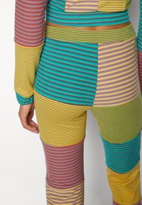 Vêtements de détente rayés multicolores avec différentes sections de patchwork en turquoise, jaune, vert pastel, violet et rouge. Matière douce et extensible.