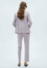 Helles lila maßgeschneidertes Anzug aus glattem Stoff; verfügt über einen taillierten Blazer mit Schlitzen und schlanken Hosen, kombiniert mit schwarzen High Heels.