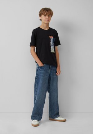Zwart t-shirt met korte mouwen, featuring een kleurrafische afbeelding op de borst, gecombineerd met losse lichtblauwe spijkerbroek en witte schoenen.