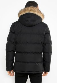 Sort pufferjakke med hætte, der har en faux fur-kant. Designet inkluderer quiltede sektioner og er lavet af et let, glat materiale.