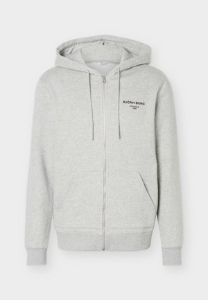Light grey zip-up hoodie with front pockets, drawstring hood, and "BJÖRN BORG Stockholm 1986" printed on the left chest.