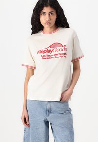 Cream t-shirt with red ribbed collar and sleeves, featuring a retro graphic print of "ReplayGoods" and Monte-Carlo Country Club text.