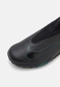 Schwarzer Slipper mit einem strukturierten synthetischen Obermaterial, das ein grünes Nike-Logo sowie eine Gummisohle mit sichtbaren Profilmustern aufweist.
