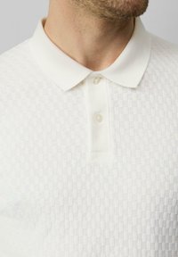 Witte polo met een gestructureerd patroon, voorzien van een klassieke kraag en een placket met drie knopen. Zachte stof voor comfort en ademend vermogen.