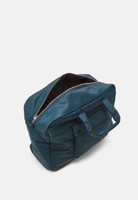 Geantă de voiaj din nylon teal, cu deschidere cu fermoar, dotată cu două mânere superioare și un buzunar frontal cu prindere prin clichet. Textură netedă și design cu umplutură.