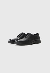 Los zapatos de cuero negro presentan una textura suave, un perfil bajo, un diseño de cordones y una suela de goma gruesa para mayor durabilidad.