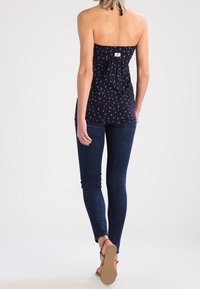 Námořnická top bez ramínek s bílým květinovým potiskem, s nařaseným detailem vzadu, spárovaný s tmavými úzkými džíny a béžovými sandály. Hladký povrch látky.