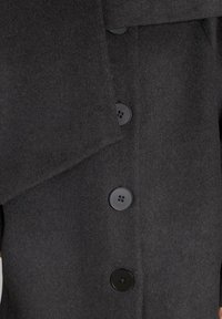 Abrigo de lana negro con un amplio cuello, cuatro botones texturizados negros y un acabado de tela suave. Las líneas simples y limpias realzan el diseño.