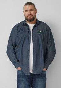 Denim overhemd met knopen in donkerblauw met lange mouwen, met een groene schildpad geborduurd met een rode hoed op de linkerborst.