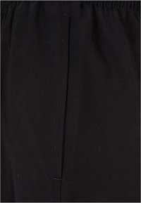 Gros plan sur un pantalon en tissu noir avec une ceinture élastique et une ouverture de poche latérale verticale avec des coutures visibles.