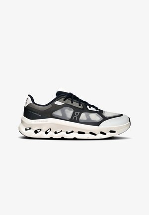 Sneaker sportiva dal profilo basso con tomaia in mesh bianco e nero, lacci neri e suola bianca spessa con ritagli neri ammortizzanti.