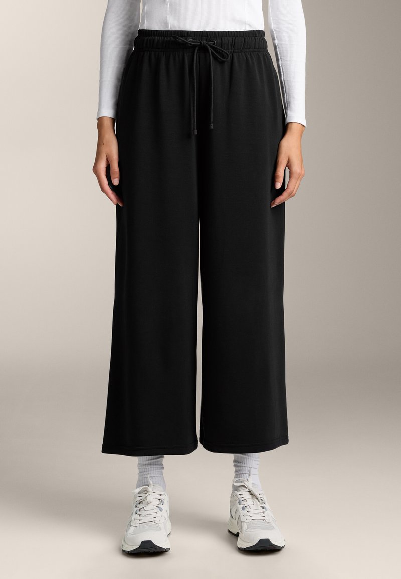 Zwarte sweatpants met wijde pijpen en een trekkoord in de taille, met een gladde textuur en een zoom die net boven de enkel valt.