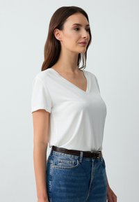 T-shirt bianca a collo a V con maniche corte, realizzata in tessuto morbido, abbinata a jeans in denim blu a vita alta e una cintura in pelle marrone.