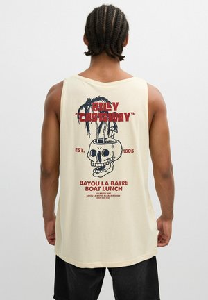 Hombre con el cabello trenzado que lleva una camiseta sin mangas de color crema con un diseño en la espalda que muestra una maceta en forma de calavera con palmeras y texto rojo.