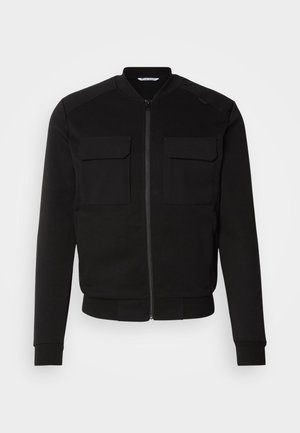 Black bomber jacket made of soft fabric features a zip front, two chest pockets, ribbed cuffs, and a cropped hem. Smooth texture and fitted design.