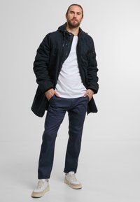 Black hooded jacket with buttons, white t-shirt, navy trousers, and cream sneakers. The jacket has a textured fabric and a casual fit.