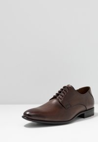 Scarpe eleganti in pelle marrone con un design elegante, punta rotonda e lacci a cinque fori. Presentano una texture liscia e una leggera cucitura tonale.