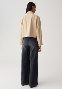Giacca cropped beige con colletto e semplici dettagli di cucitura, abbinata a jeans in denim scuro a vita alta e gamba larga.