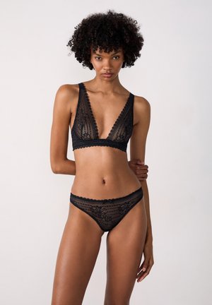 Brassiere in pizzo nero con scollatura a V profonda e bordi scallop, abbinato a uno slip in pizzo coordinato con un delicato motivo floreale.