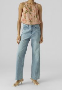 Top floreale senza maniche in rosa chiaro, abbinato a jeans a gamba larga blu chiaro. Tacchi trasparenti completano il look.