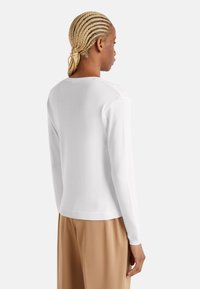 Maglione bianco a maniche lunghe in maglia con colletto rotondo, polsini e orlo a coste. Il design sul retro presenta dettagli delle cuciture.