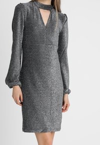 Glittrande silverfärgad långärmad klänning med nyckelhålsutskärning och lätt puffade ärmar som slutar i samlade manschetter, knälängd passform.