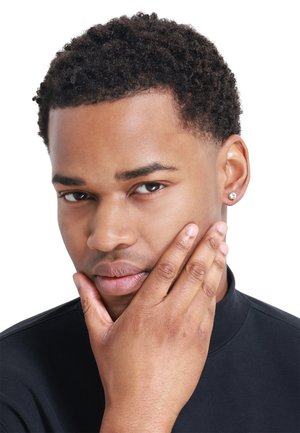Close-up of a person with short, curly black hair wearing a black top. They have a single stud earring and are touching their chin with one hand.