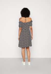 Vestido preto às riscas com padrão floral branco, cintura franzida, mangas curtas em balão e comprimento até ao joelho; combinado com ténis brancos.
