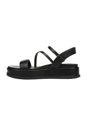Black sandal made of synthetic material. Features flat sole, wide front strap, and multiple slender straps crossing over the instep.