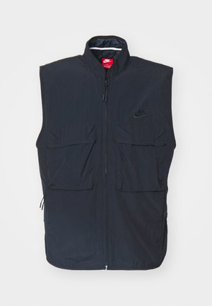 Navy sleeveless vest made of lightweight material, featuring a high collar, front zipper, and two large patch pockets. Subtle logo detail.