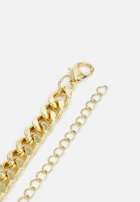 Bracelet en chaîne dorée avec des maillons entrelacés, fermoir en forme de homard et chaîne d'extension réglable pour varier les tailles.