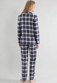 Marineblauwe en witte geruite pyjama set met lange mouwen en broek, gemaakt van een zachte stof met een gladde textuur. Casual ontwerp zonder opvallende details.
