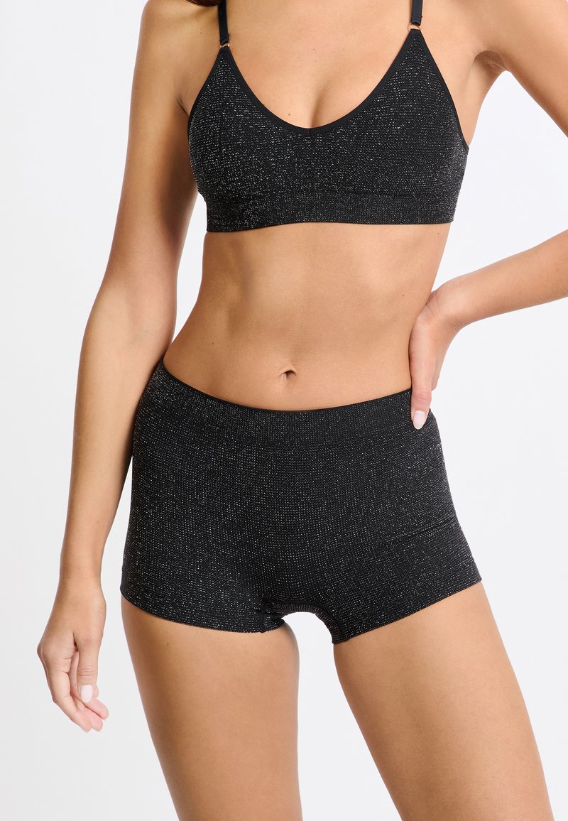 Sujetador negro y pantalones cortos de cintura alta a juego, hechos de una tela texturizada con acentos metálicos, con un diseño simple y sin cierres.