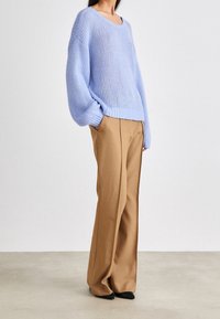 Ljusblå stickad tröja med vid halsringning och lösa ärmar, matchad med ljusbruna högmidjade byxor och svarta spetsiga skor.