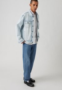 Light blue denim jacket with two chest pockets, gray striped shirt underneath, relaxed-fit blue jeans, and black loafers.