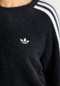 Sweatshirt preto de polar com três riscas brancas nas mangas e um pequeno logotipo bordado em branco no peito.