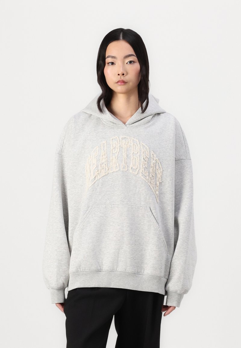 Grå oversized hoodie med en frontlomme og et tekstureret beige "HEARTBEAT" grafik på brystet. Blødt stof og vide ærmer.
