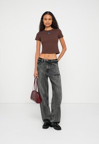 Brun kort t-shirt med liten logotyp, grå vida jeans, svarta skor och en röd handväska. Mjuk tyg och avslappnad passform.