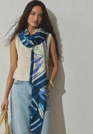 Modrý šál s abstraktnými vzormi v odtieňoch modrej, bielej a zelenej, vyrobený z mäkkej tkaniny, ovinutý okolo krku.