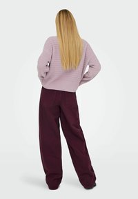 Pull en lilas tricoté avec un design texturé, associé à un pantalon bordeaux ample. L'ensemble présente une silhouette décontractée et des matériaux doux.