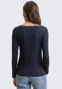 Marineblauwe longsleeve shirt met een brede halslijn, geribbelde textuur en een aansluitend ontwerp, gecombineerd met lichtblauwe denim jeans.