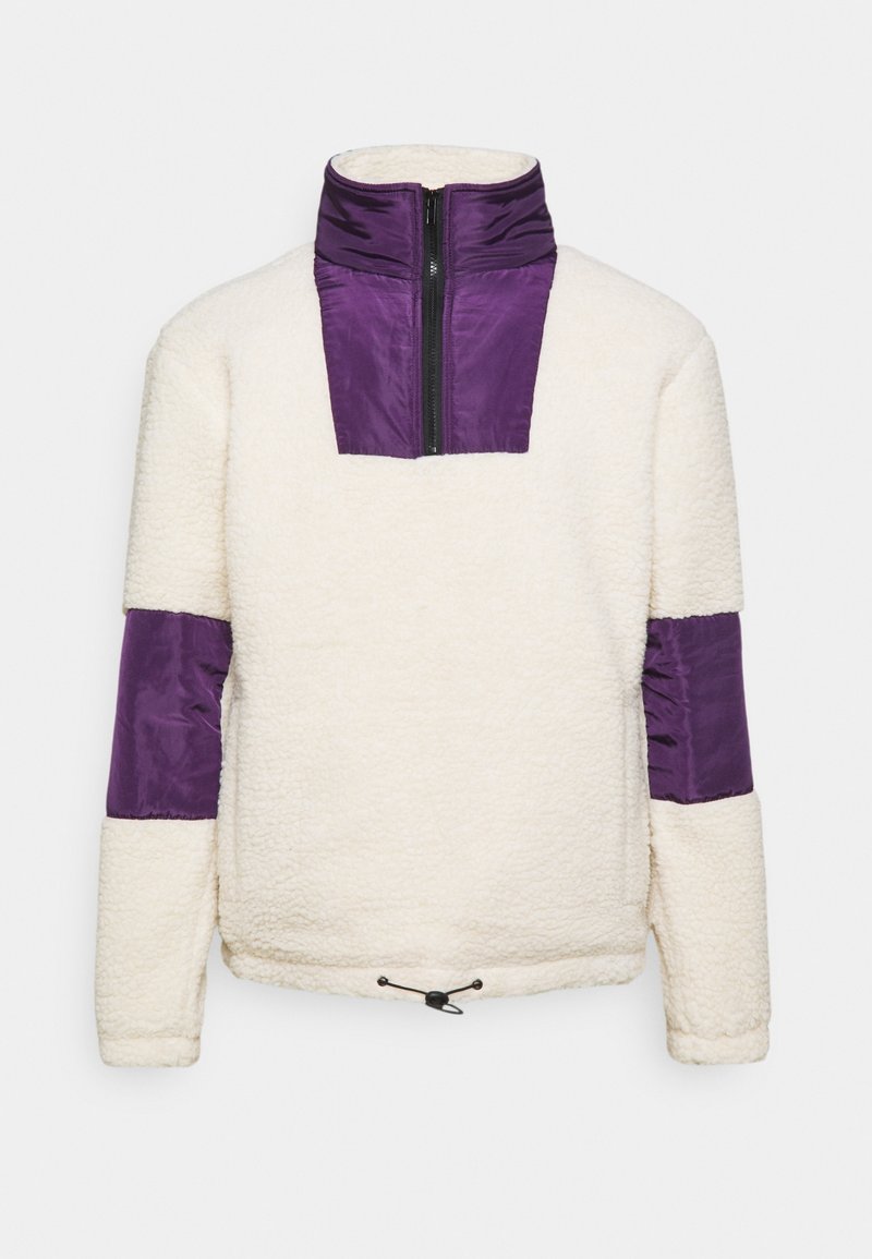 Bluza polarowa w kremowym kolorze z fioletowym nylonowym kołnierzem i akcentami na rękawach. Posiada półzamek z przodu oraz regulowany ściągacz na dole.