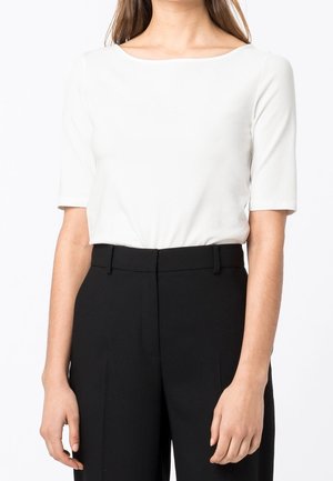 Hvid kortærmet top med firkantet halsudskæring, lavet af glat stof, parret med højtaljede sorte skrædderbukser.