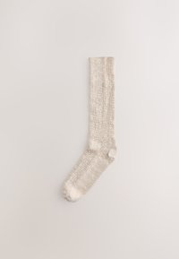 Chaussette haute jusqu'au genou de couleur beige clair avec une texture côtelée et une finition douce, dotée d'un talon et d'un bout renforcés pour une meilleure durabilité.