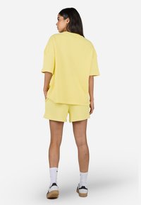Žluté žebrované oversized tričko spárované s odpovídajícími šortkami, s krátkými rukávy, uvolněným střihem a bílými sportovními ponožkami se sneakers.