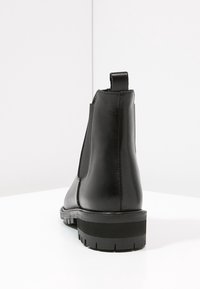 Czarne skórzane botki za kostkę o gładkim wykończeniu, z elastycznymi panelami bocznymi i grubą gumową podeszwą z teksturowanym wzorem zapewniającym przyczepność.